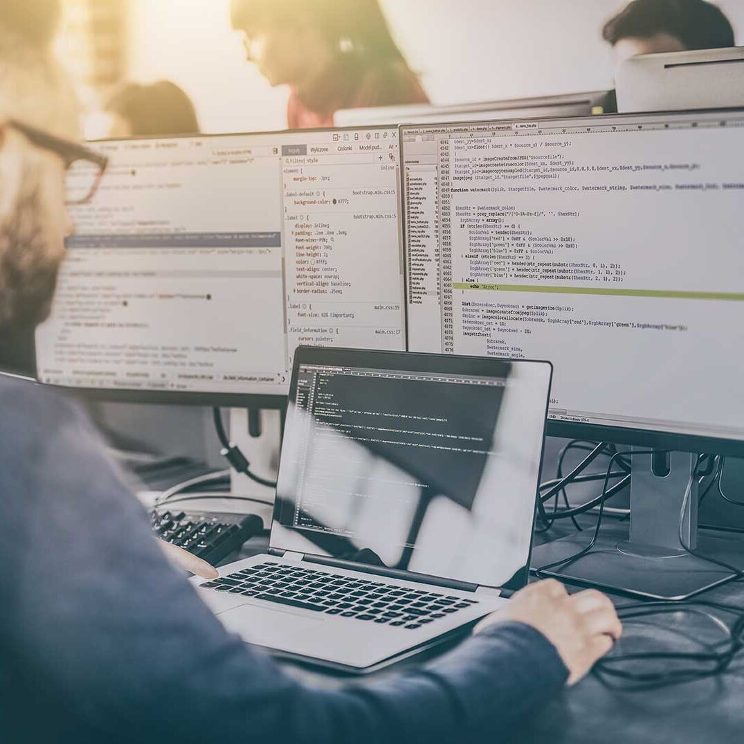 Entwickler sitzt vor MacBook mit zwei Bildschirmen